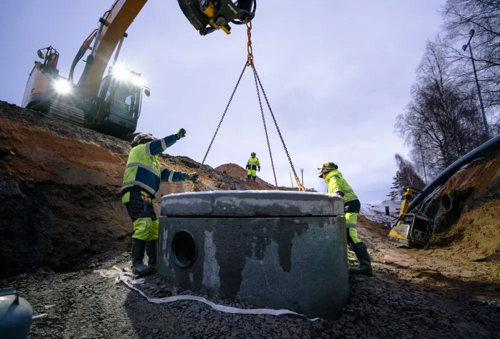Työntekijät asentamassa betonikaivoa työmaalla nosturin avulla